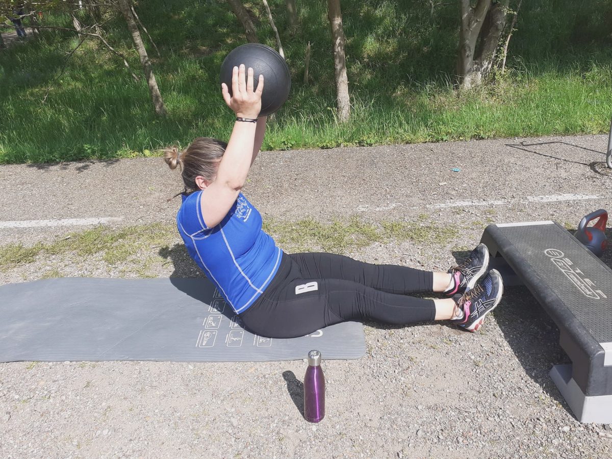 Iemand houdt een medicinebal vast op een pad langs het water tijdens een training