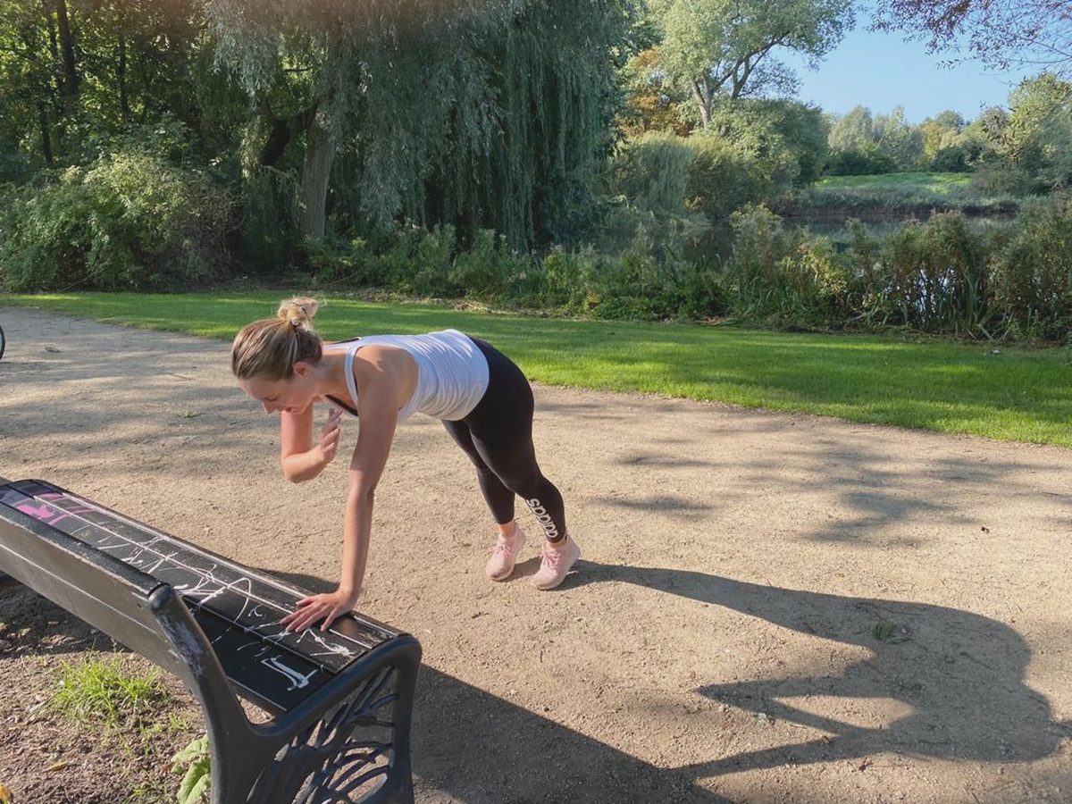 Iemand doet een oefening tegen een bankje op een pad in een park