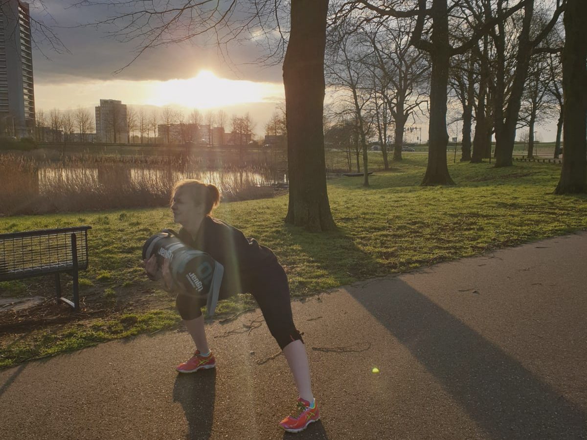 Iemand traint bij zonsopgang in een park, met de zon laag achter de bomen